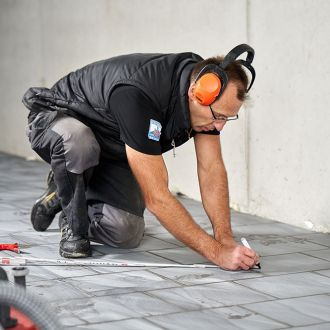 Handwerker markiert keramische Bodenfliesen für weitere Arbeiten am Rüttelbelag